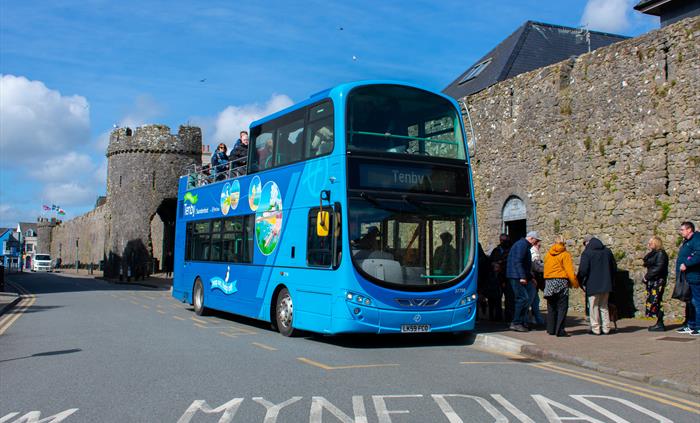 an open-top bus dropping off passengers at a bus stop